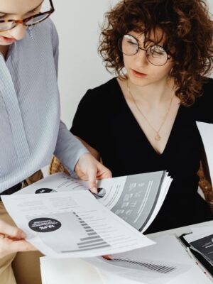 Two women review and discuss financial documents in an office setting, highlighting teamwork and analysis.