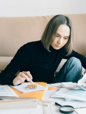 Young woman handling financial tasks with papers and laptop in cozy living room.